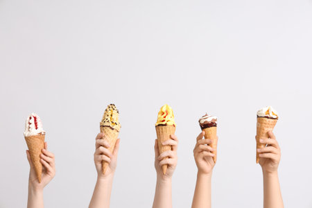 Female hands with different sweet ice-cream in waffle cones on gray backgroundの写真素材