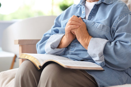 Senior woman with Bible praying at home, closeup