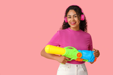 Happy African-American woman with water gun on pink backgroundの写真素材