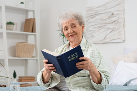 Senior woman on bed reading Bible at homeの写真素材