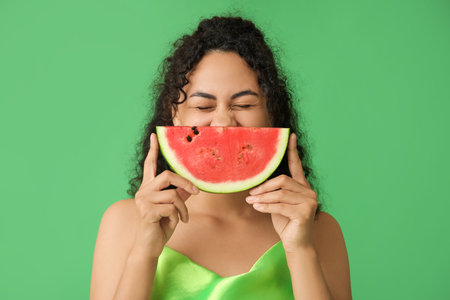 Happy young African-American woman with fresh watermelon on green backgroundの写真素材