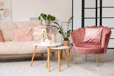 Cozy sofa with cushions, armchair and coffee table with flowers in interior of living room