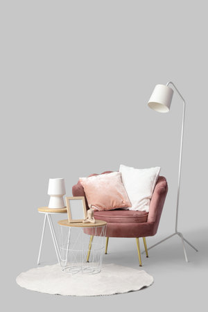 Armchair with cushions, lamp and coffee tables with frame and vase on gray backgroundの写真素材