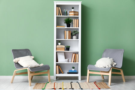 Bookcase with books and houseplants near cozy armchairs in living roomの写真素材