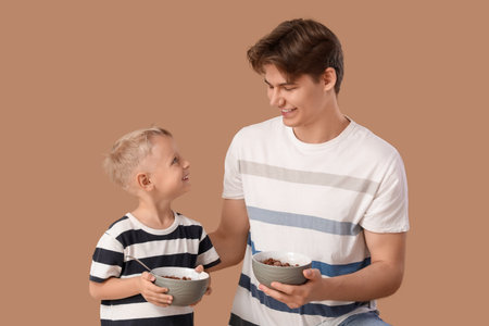Happy father and his little son with bowls of cornflakes on brown backgroundの写真素材