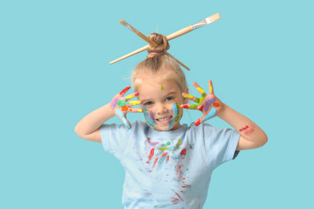 Cute little girl in paint with brushes on blue backgroundの写真素材