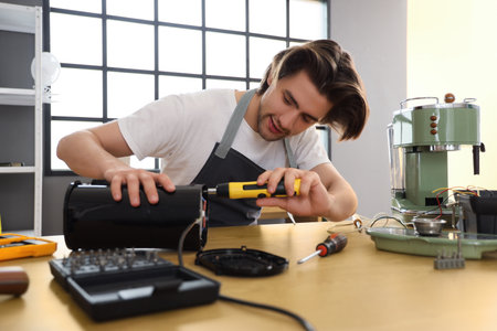 Male worker with screwdriver repairing coffee machine at table in workshopの写真素材