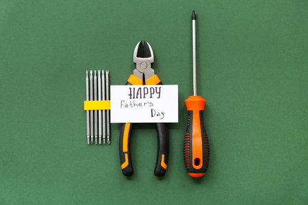 Pliers, screwdriver, bits and greeting card with text HAPPY FATHER'S DAY on green background