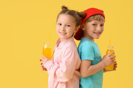 Cute children with bottles of lemonade on yellow backgroundの写真素材