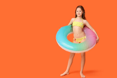 Cute little happy girl in swimsuit with inflatable ring on orange backgroundの写真素材