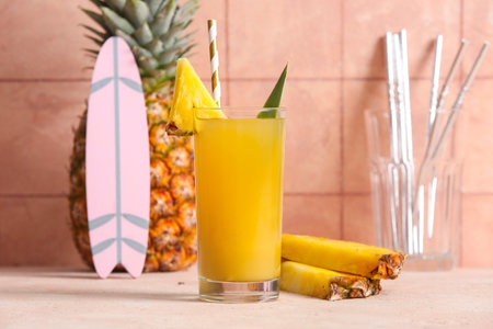 Fresh ripe pineapple with glass of tasty juice and mini surfboard on table near pink tile wallの写真素材