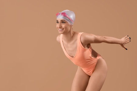Happy young female swimmer posing on beige backgroundの写真素材