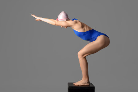 Happy young female swimmer on springboard against gray background, side viewの写真素材