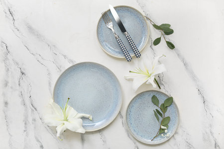 Beautiful composition with blue clean plates, flowers and cutlery on marble table