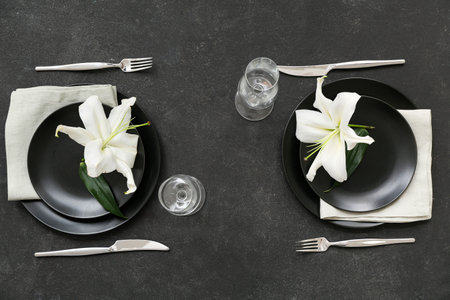 Beautiful table setting with black plates, cutlery, champagne glasses and flowers on dark backgroundの写真素材