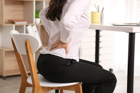 Young businesswoman suffering from back pain on chair at office, closeup