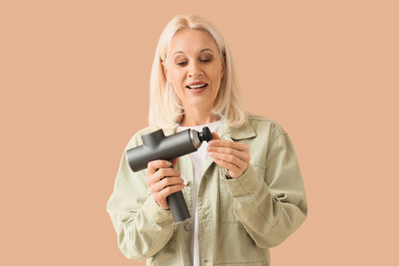 Mature woman with percussive massager on beige background