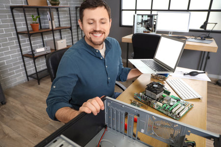 Male technician with laptop repairing computer unit on table in service centerの写真素材