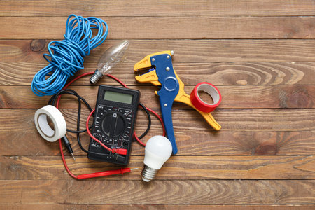 Set of electrician's tools, light bulbs and cable on wooden background