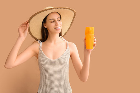 Beautiful young woman with bottle of sunscreen cream on brown background