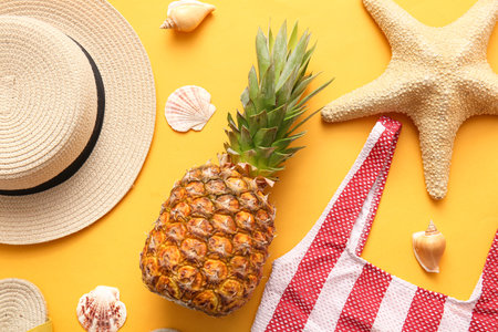 Fresh pineapple with wicker hat, swimsuit, starfish and shells on orange background