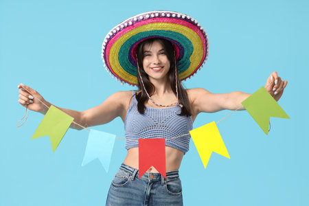 Young woman with colorful sombrero and bunting on blue background. Cinco de Mayo celebrationの写真素材
