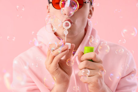 Cool young man blowing soap bubbles on pink background, closeupの写真素材