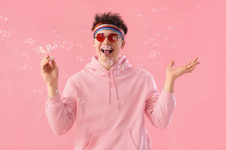 Cool young man blowing soap bubbles on pink background