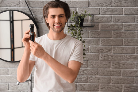 Young bearded man with trimmer in bathroom