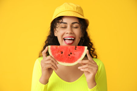 Happy young African-American woman with fresh watermelon on yellow backgroundの写真素材