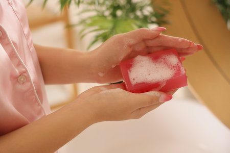 Young woman with soap near sink in bathroom, closeup