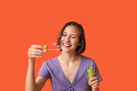 Happy teenage girl with soap bubbles on orange background