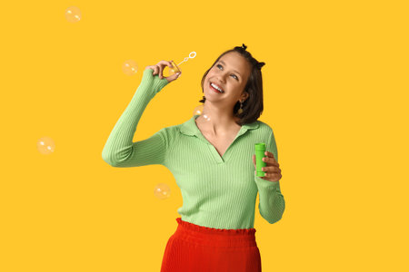 Teenage girl blowing soap bubbles on yellow background