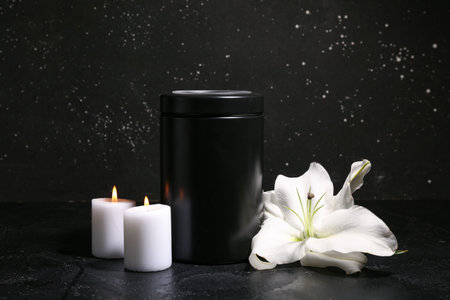 White flower, candles and mortuary urn on black backgroundの写真素材