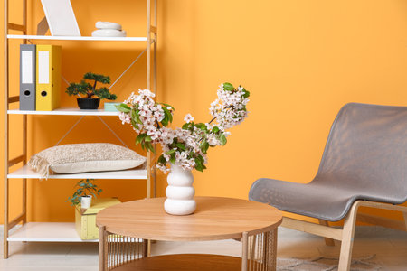 Vase with blossoming branches on coffee table near orange wall in living roomの写真素材