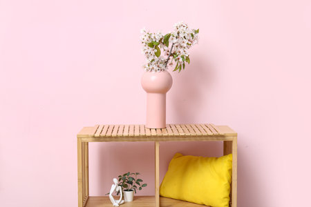 Vase with blossoming branches on shelf near pink wall in roomの写真素材