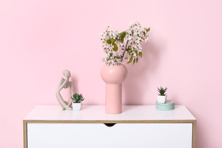 Vase with blossoming branches on table near pink wall in roomの写真素材