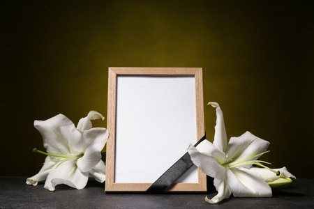 Blank funeral photo frame and flowers on dark backgroundの写真素材