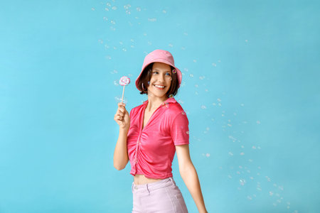 Teenage girl with sweet lollipop and soap bubbles on blue background