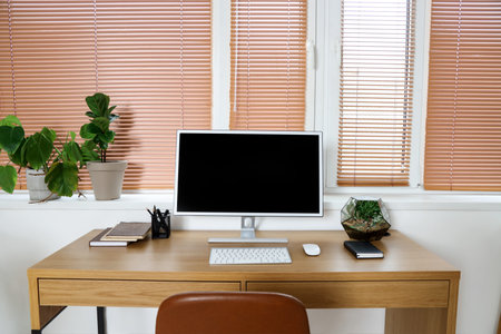 Workplace with computer monitor and green houseplants near window in officeの写真素材