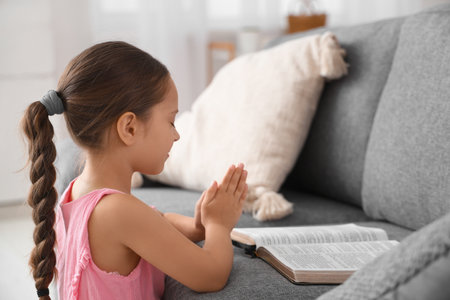 Cute little girl with open Bible praying at homeの写真素材