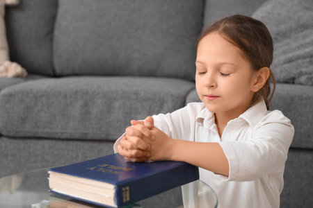 Cute little girl with Bible praying at homeの写真素材