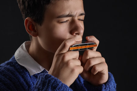 Teenage boy playing harmonica on black background, closeupの写真素材