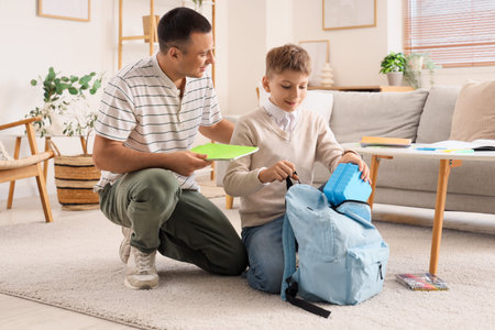 Little boy with his father packing school lunchbox into backpack at homeの写真素材