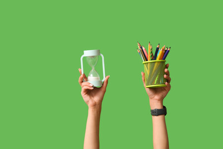Female hands with stationery and hour glass on green background
