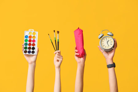 Many hands with palette, brushes and alarm clock on yellow backgroundの写真素材