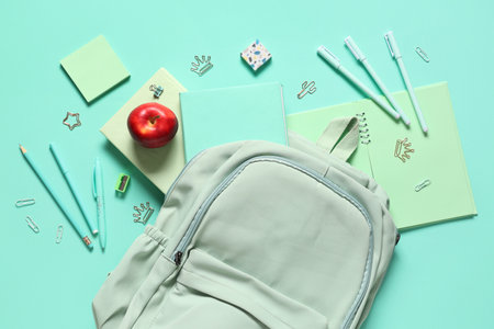 Tasty red apple, backpack and different school stationery on turquoise backgroundの写真素材