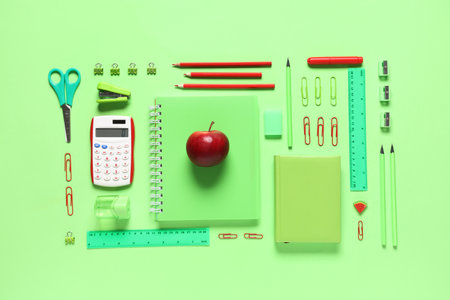 Tasty red apple and different school stationery on green backgroundの写真素材