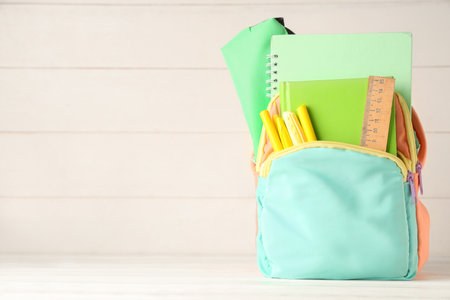 Backpack with school supplies on table against wooden white backgroundの写真素材