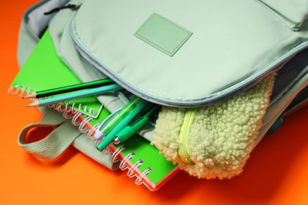 Backpack with school supplies on orange background